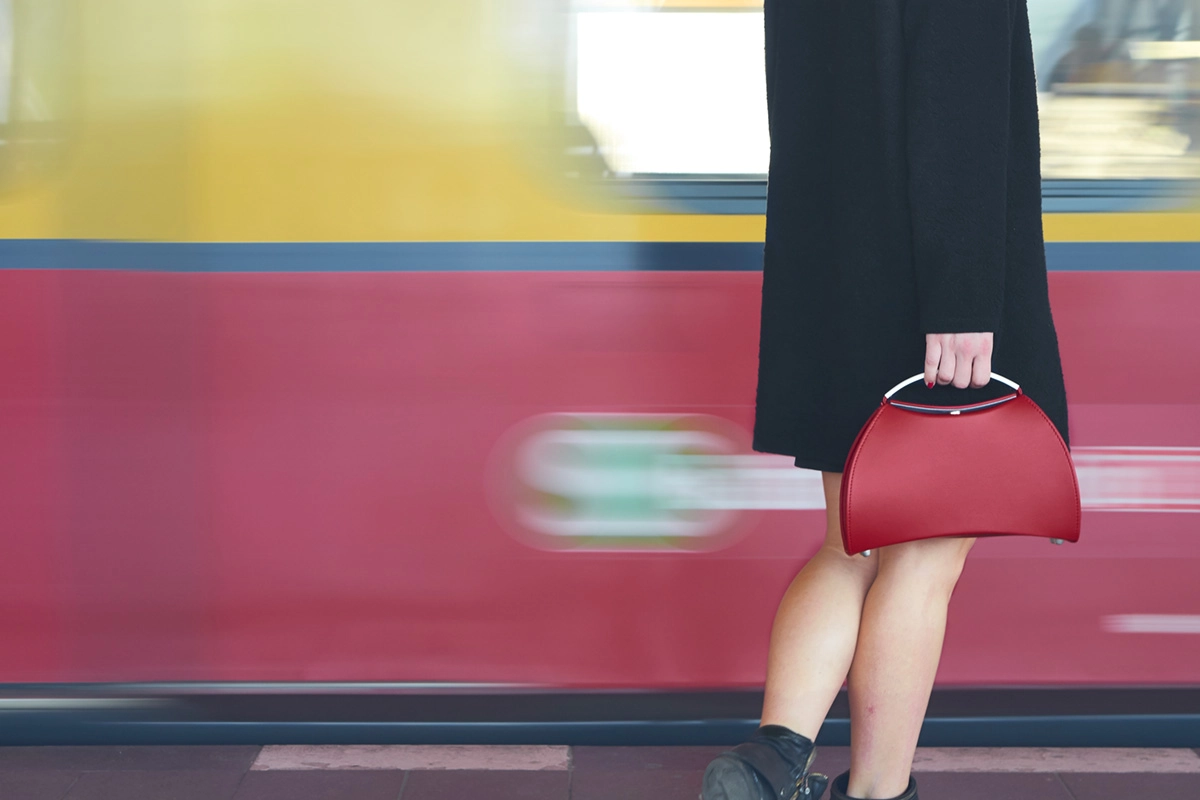 Frau mit schwarzem Mantel und rotem Olbrish Handtasche steht vor eingefahrener S-Bahn in Berlin