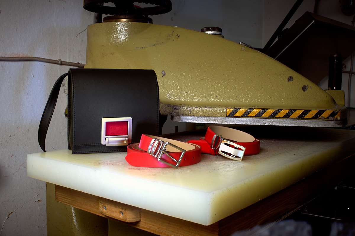 Olbrish Handbag Square in schwarz-rotem Nappaleder und zwei rote Gürtel auf dem Arbeitsbank einer alten DDR-Stanze