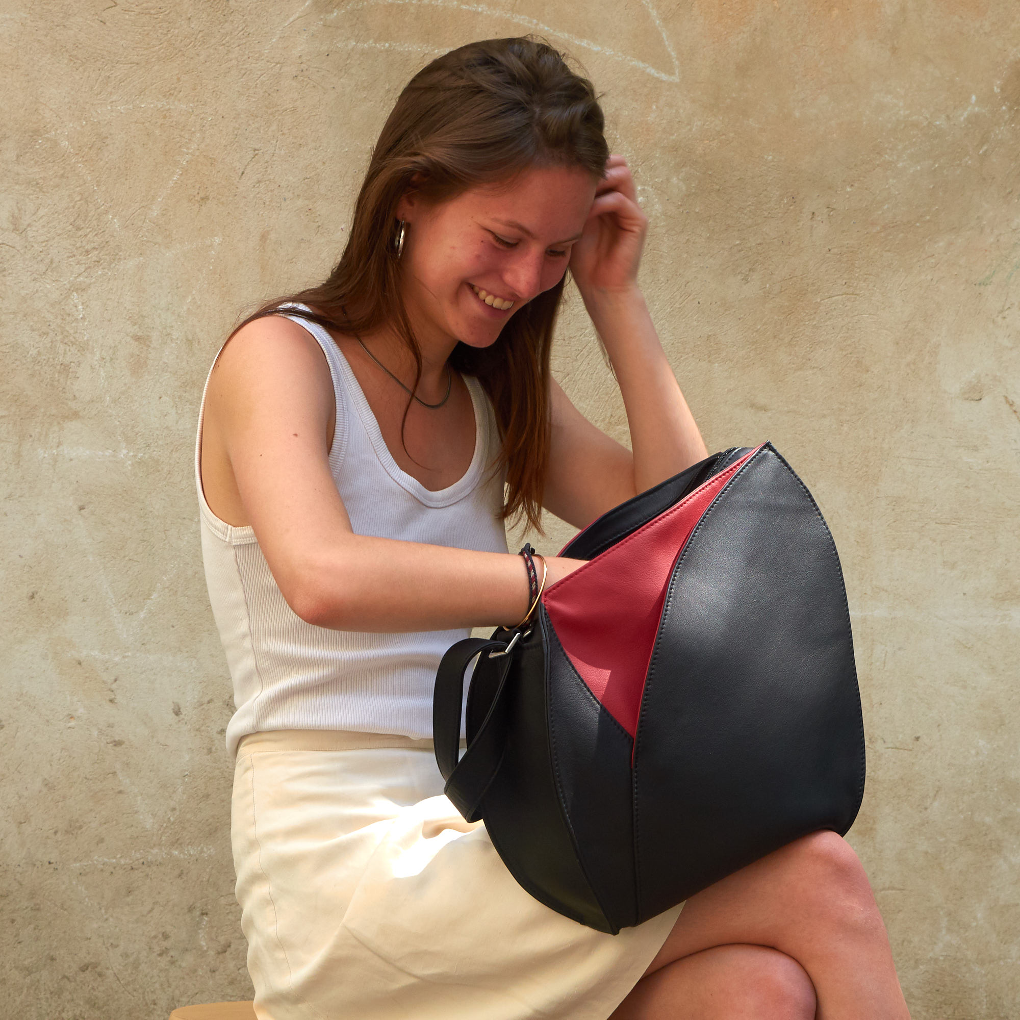 Lächelnde Frau sucht in Olbrish Handtasche Flora aus schwarz-rotem Nappaleder